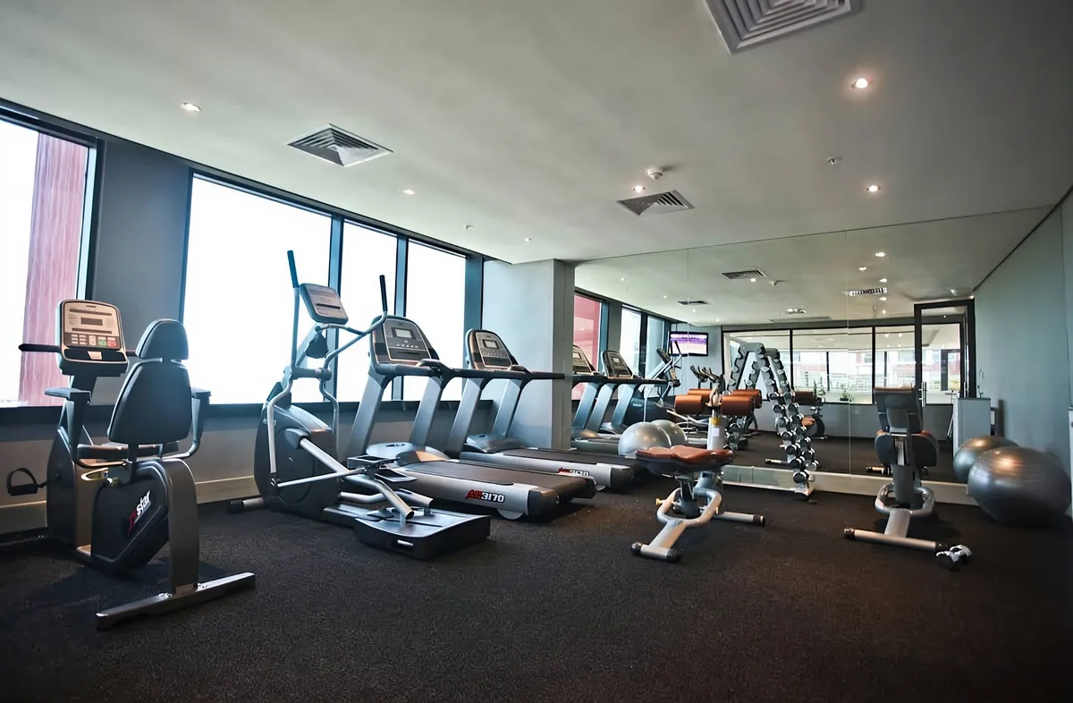 Hotel fitness centre with treadmills, cross trainers and free weights along a window wall