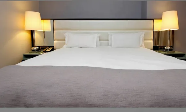 King bed dressed in white linen between matching bedside lamps